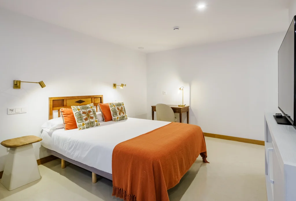 Cama doble en dormitorio completo de estilo minimalista y detalles naranjas